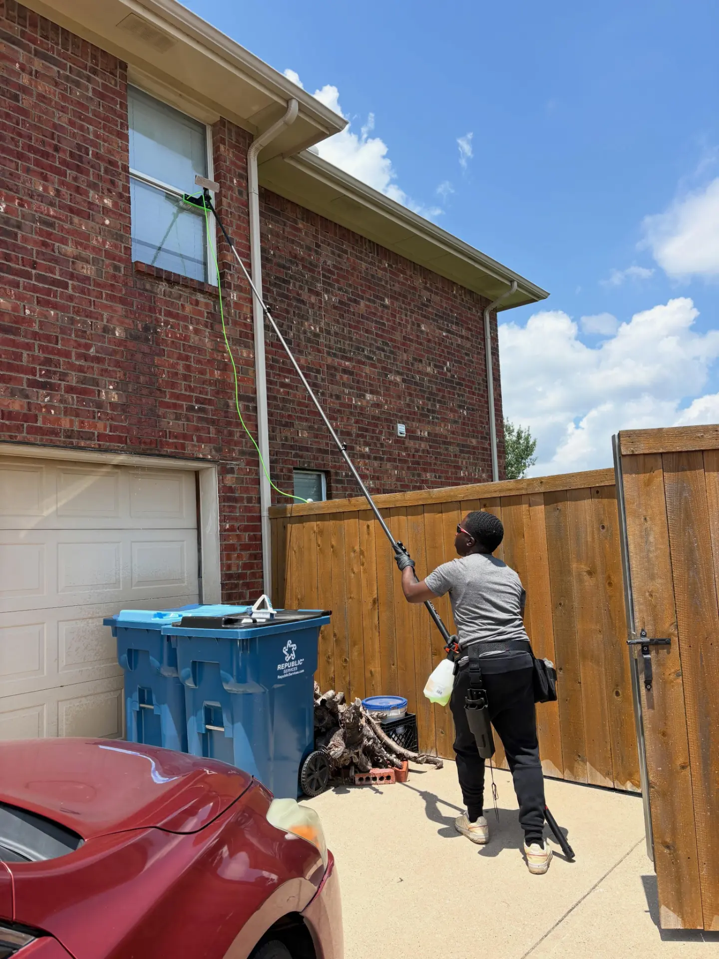 Total Surface Care technician cleaning upstairs windows on a brick home in the Dallas-Fort Worth area