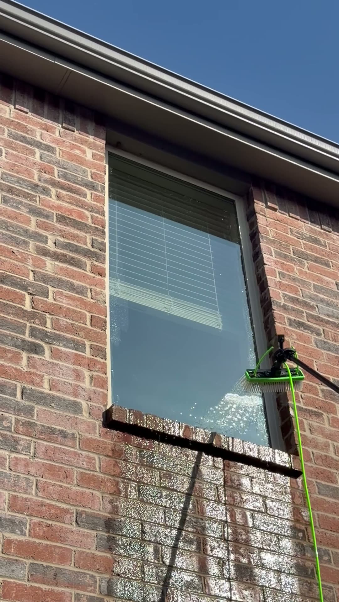Squeegee pulling water down a soapy window on a red brick home
