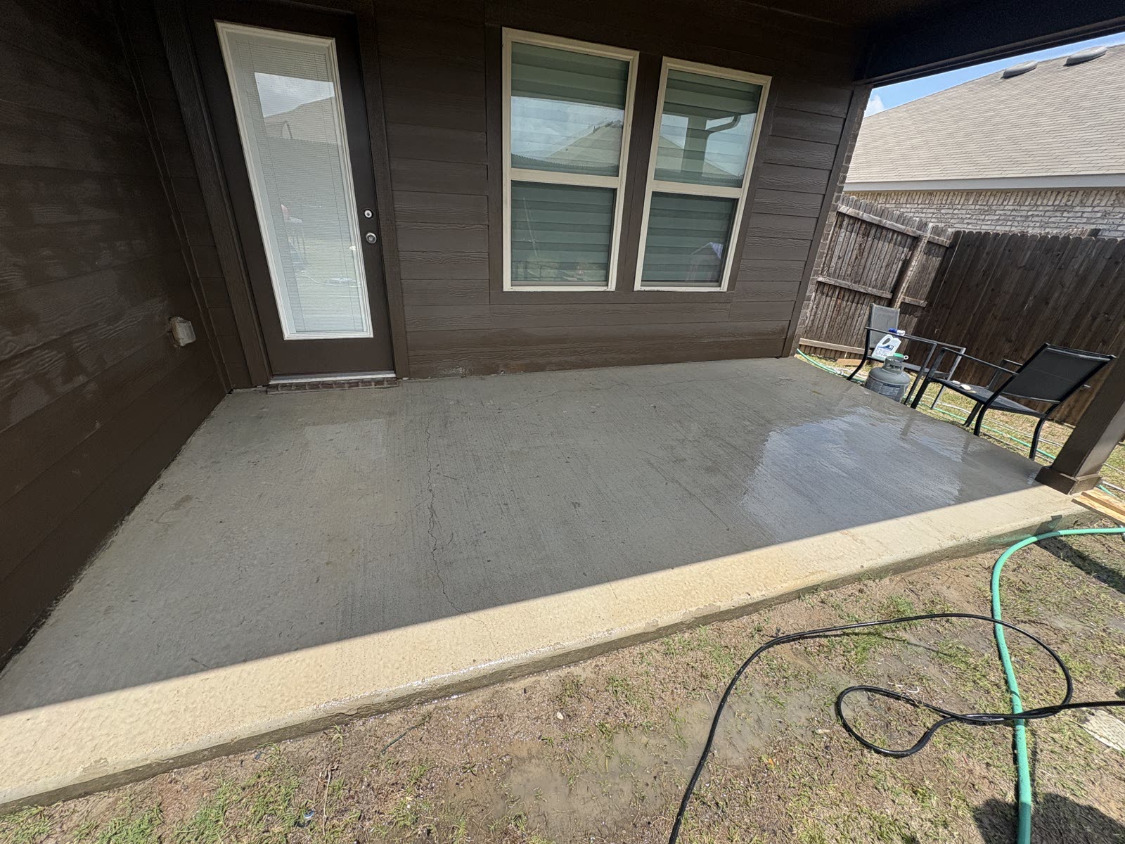 Covered concrete patio at a home before washing, with a hose laid out