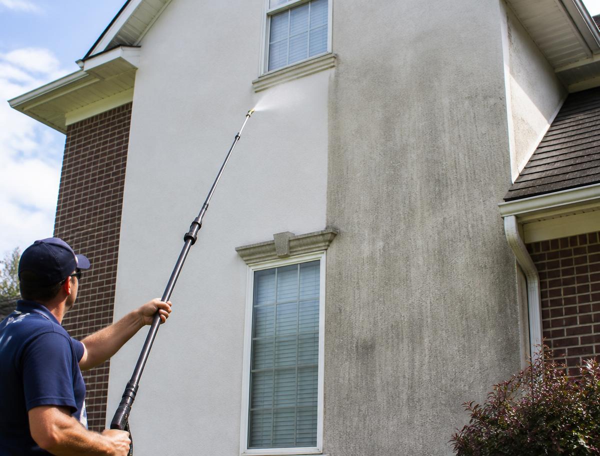 Exterior house wall being rinsed clean, showing the difference against the unwashed section